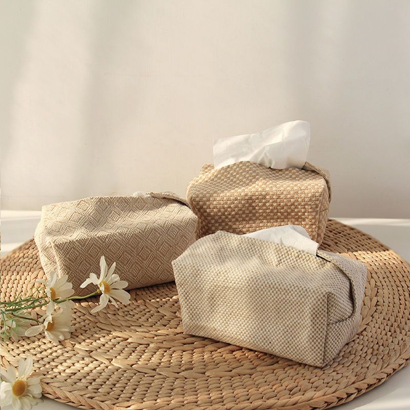 Three neutral textured fabric tissue box covers displayed together on a woven mat