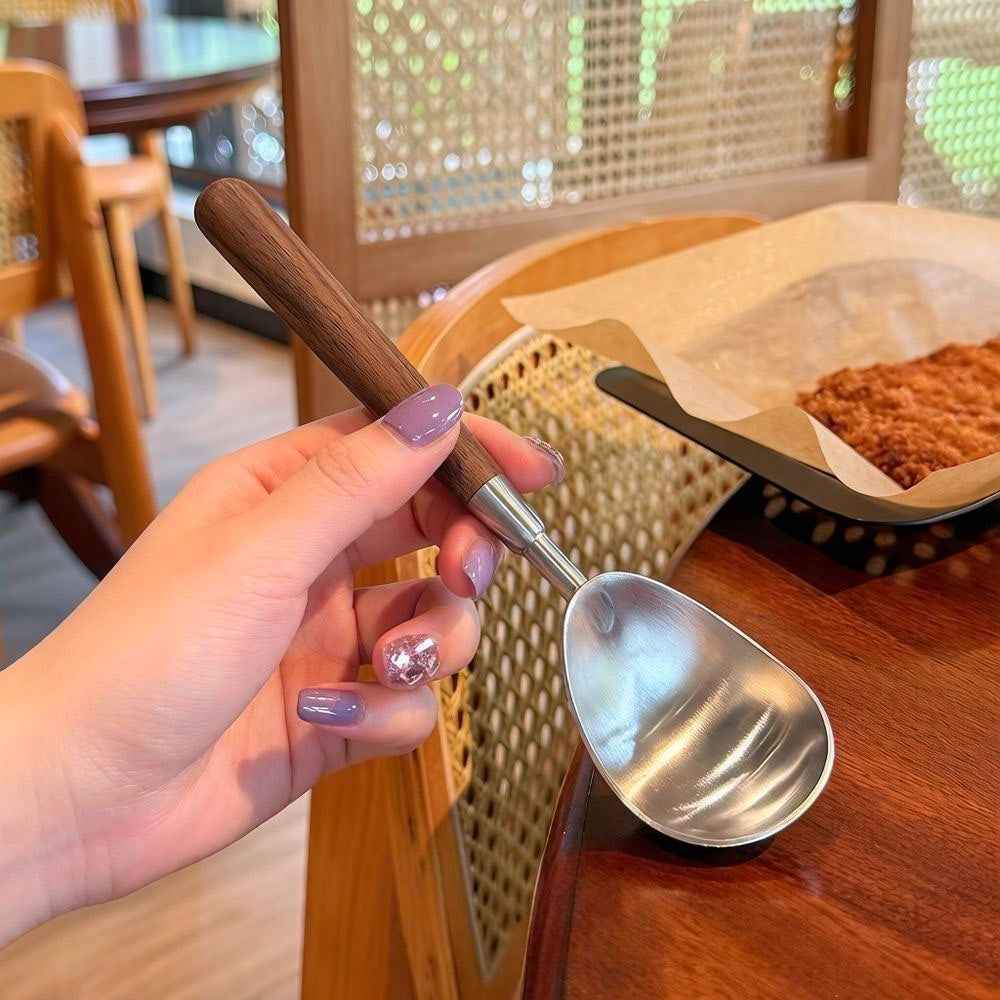 Close-up of the walnut-style handle and stainless steel scoop on a fruit serving table.