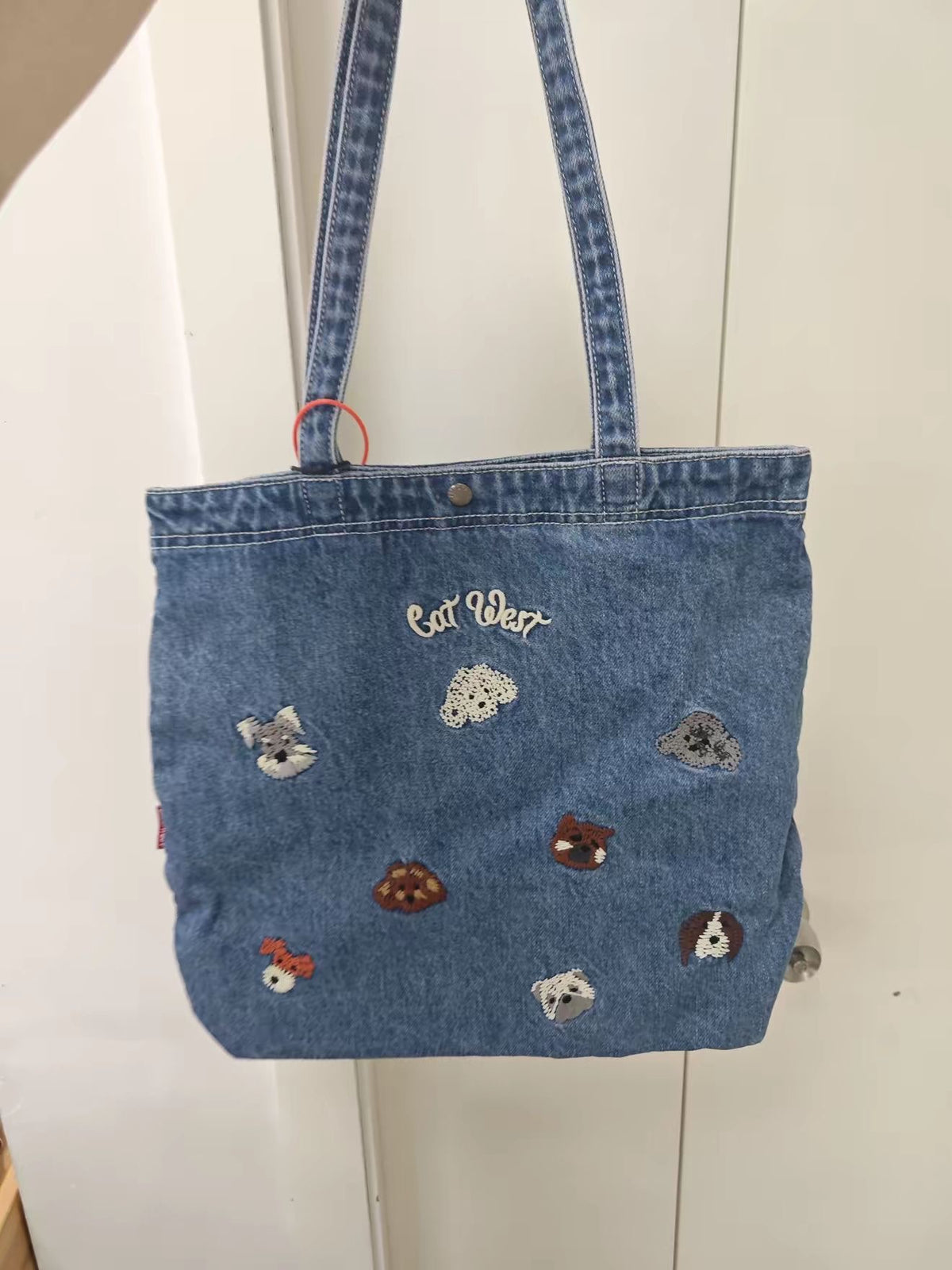 Blue denim shoulder tote with embroidered animal motifs, shown upright