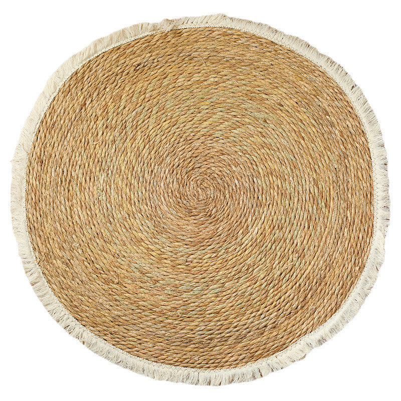 Round handwoven straw mat with cream fringe on white background